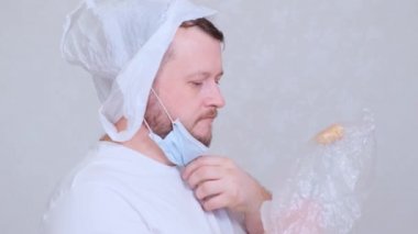 Kafasında çuval olan sakallı bir adam ve koruyucu bir maskede çatal pirzola var. Enfeksiyon korkusu. Coronavirüs COVID-19 salgını, evde kendini izole etme ve karantina. 