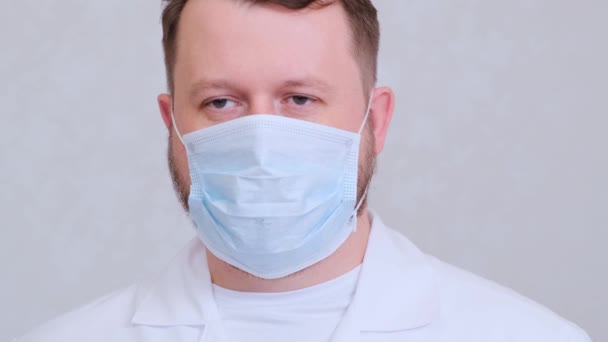 保護マスクの男性と白いシャツは、カメラ、クローズアップを見ています。衛生概念。細菌や細菌の拡散を防ぎ王冠ウイルスへの感染を防ぎ — ストック動画