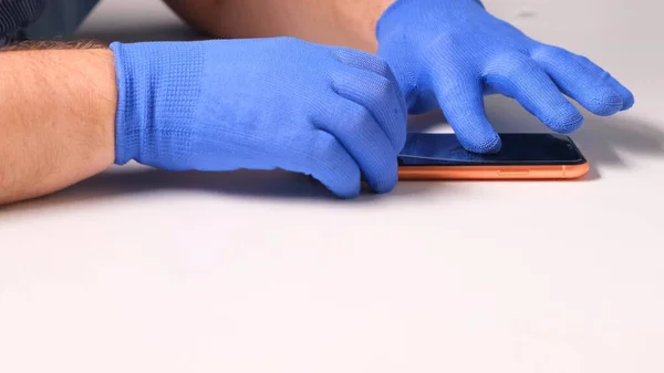 Mãos masculinas em luvas azuis substitui um protetor de tela de vidro temperado quebrado para um smartphone. Um homem prepara um smartphone para substituir o vidro. Conceito de reparação Smartphone. espaço de cópia — Fotografia de Stock