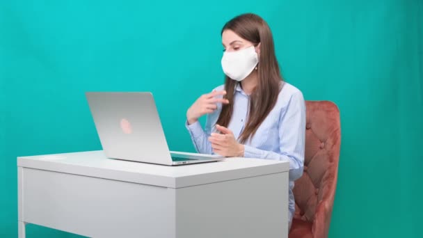 Das Weibchen in Schutzmaske spricht während einer Pandemie am Arbeitsplatz oder zu Hause per Videolink auf einem Laptop. Das Konzept der Arbeit während Quarantäne und Selbstisolierung. — Stockvideo