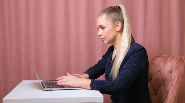 Mulher está usando laptop enquanto está sentado em sua mesa. Jovem empresária europeia está sentada no escritório e trabalhando em software notebook . — Fotografia de Stock