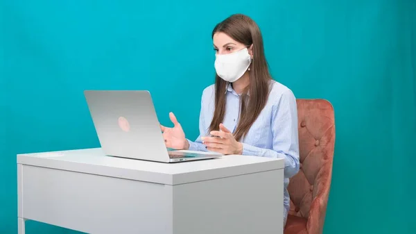 Das Weibchen in Schutzmaske spricht während einer Pandemie am Arbeitsplatz oder zu Hause per Videolink auf einem Laptop. Das Konzept der Arbeit während Quarantäne und Selbstisolierung. — Stockfoto