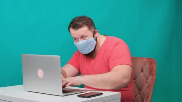 男性使用笔记本电脑的滑稽画面。戴着防护性医疗面具在电脑上工作的人，假扮黑客. — 图库视频影像