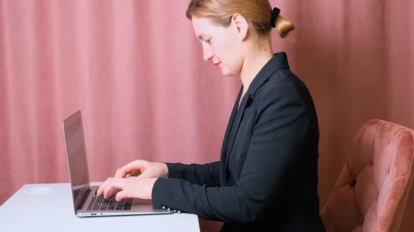 Серйозна жіноча секретарка, що друкує на ноутбуці, сидить за столом на своєму робочому місці . — стокове фото