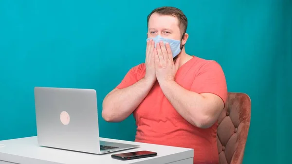 Pembe tişörtlü sakallı adam evdeki laptopta yeşil arka planda çalıştığı için koruyucu bir tıbbi maske takıyor. Erkek şaşırdı. Karantina konsepti — Stok fotoğraf