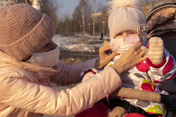 Dziewczyna z dzieckiem stoi na drodze w ochronnej masce medycznej. Mama poprawia maskę ochronną dla córki. Gęsty smog na ulicach. Epidemia grypy. — Zdjęcie stockowe