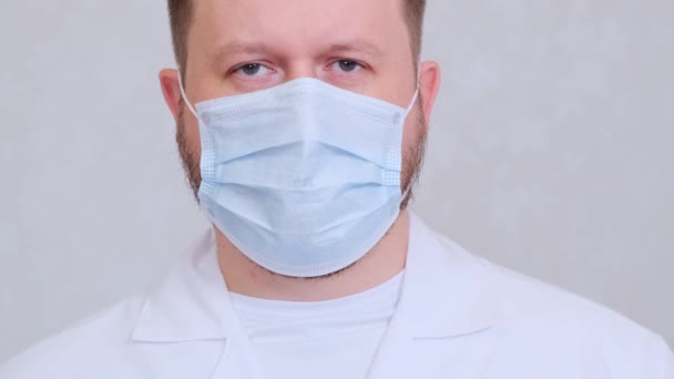 Hombre con una máscara protectora y una camisa blanca mira a la cámara, de cerca. Concepto de higiene. prevenir la propagación de gérmenes y bacterias y evitar la infección con el virus de la corona — Vídeos de Stock