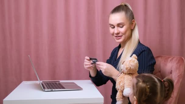 Jeune belle blonde et sa charmante petite fille font du shopping en ligne avec un ordinateur portable et une carte de crédit. Shopping dans la boutique en ligne . — Video