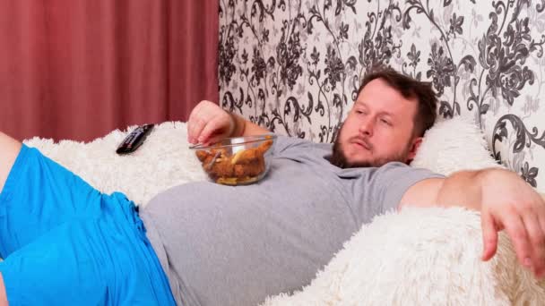 kövér ember nagy hasa fekszik a kanapén gyors ételek és unatkozik a TV előtt a távirányító a kezében, közelkép.
