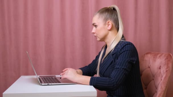 Secretária séria digitando em um laptop sentado em uma mesa em seu local de trabalho . — Vídeo de Stock