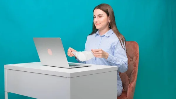 Feminino no link de vídeo em um laptop mostra uma apresentação para uma máscara médica protetora, tentando vendê-lo, no local de trabalho ou em casa durante uma pandemia. O conceito de quarentena e auto-isolamento — Fotografia de Stock