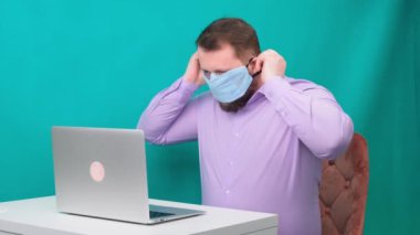 Laptopta koruyucu maske takan sakallı bir adamın portresi. Erkek kameraya bakıyor.