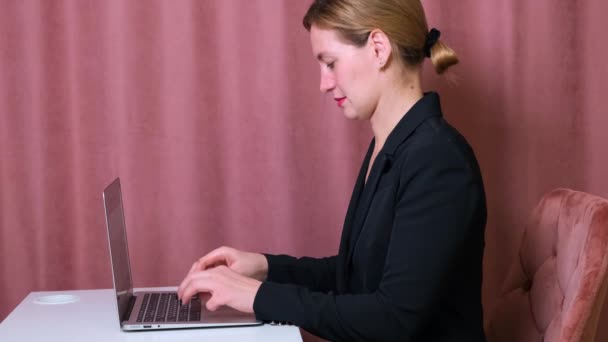 Allvarlig kvinnlig sekreterare skriva på en bärbar dator sitter vid ett bord på sin arbetsplats. — Stockvideo