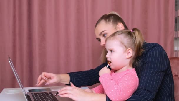 Die junge schöne Blondine und ihre charmante kleine Tochter kaufen mit Laptop und Kreditkarte online ein. Einkaufen im Online-Shop. — Stockvideo