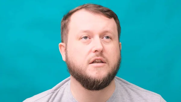 Retrato de un hombre barbudo maldiciendo enojado sobre un fondo azul . — Foto de Stock