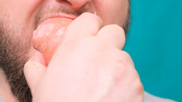 El hombre barbudo muerde comiendo una salchicha grande de salami. Concepto de dieta fallido, fuerza de voluntad en la nutrición, comida chatarra . — Foto de Stock