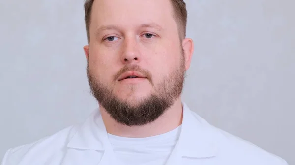 Skäggig manlig läkare i vita kläder ser sorgsen trött ut. — Stockfoto