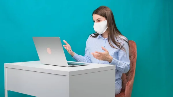 Das Weibchen in Schutzmaske spricht während einer Pandemie am Arbeitsplatz oder zu Hause per Videolink auf einem Laptop. Das Konzept der Arbeit während Quarantäne und Selbstisolierung. — Stockfoto