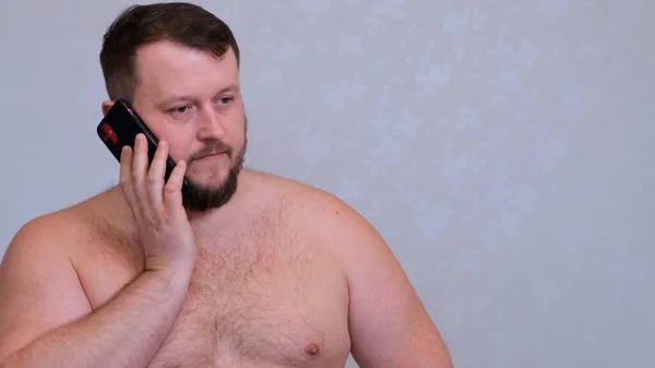 Толстый голый бородатый мужчина разговаривает по телефону, получает плохие новости, шокирован безумным злым жестом . — стоковое фото