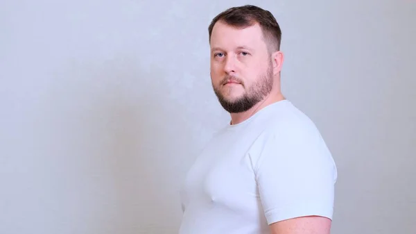 Portret de aproape al unui bărbat gras caucazian cu ochi verzi privind direct la cameră, purtând un tricou alb, expresie suspicioasă sceptică, emoție — Fotografie, imagine de stoc