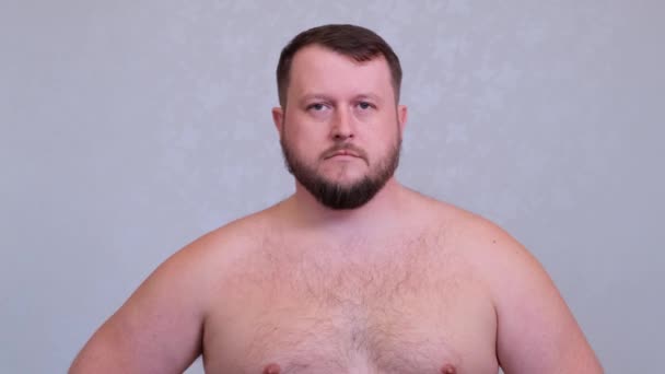 Retrato de un gordo barbudo desnudo sobre un torso sobre un fondo gris . — Vídeos de Stock