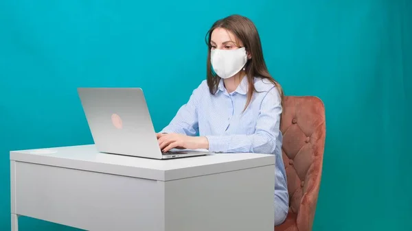 Die Frau mit Schutzmaske arbeitet während einer Pandemie am Laptop am Arbeitsplatz oder zu Hause. Das Konzept der Arbeit während Quarantäne und Selbstisolierung — Stockfoto