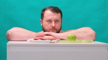 Yetişkin şişman bir adam sosis ya da yeşil elma arasında seçim yapar. Ayartılmaya karşı direnç, fast food, sağlıklı beslenme, diyet, vücut bakımı.