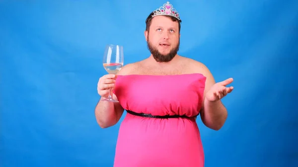 Cara barbuda engraçada em um vestido rosa feito de travesseiros bebe vinho de um copo em um fundo azul. Quarentena maluca. Moda 2020. Põe uma almofada. Desafio 2020 devido ao isolamento da casa — Fotografia de Stock