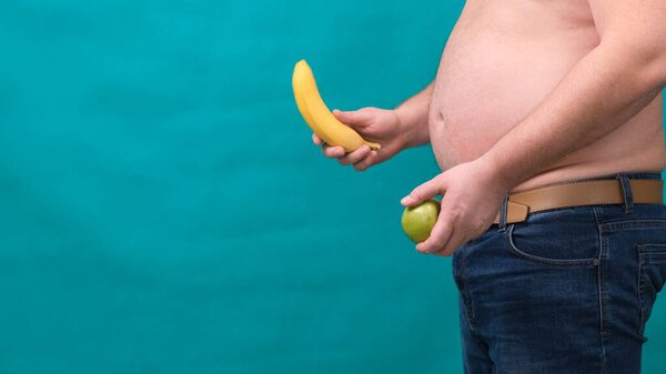 fat man with a big belly holds a green apple and a banana in his hands. The concept of healthy eating and losing weight, diet.