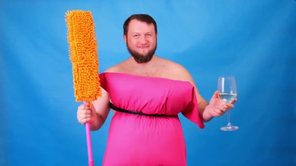 Vicces szakállas fickó rózsaszín párnaruhában, felmosóval és egy pohár borral, kék háttérrel. Őrült karantén. Vicces háztakarítás. Divat 2020. Vegyél fel egy párnát. 2020-as kihívás a háztartás miatt — Stock videók