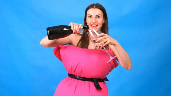 Najpiękniejsza dziewczyna w różowej sukience z poduszek nalewa szampana do szklanki na niebieskim tle. Szalona kwarantanna. Moda 2020. Załóż poduszkę. Wyzwanie 2020 ze względu na izolację domów. — Zdjęcie stockowe