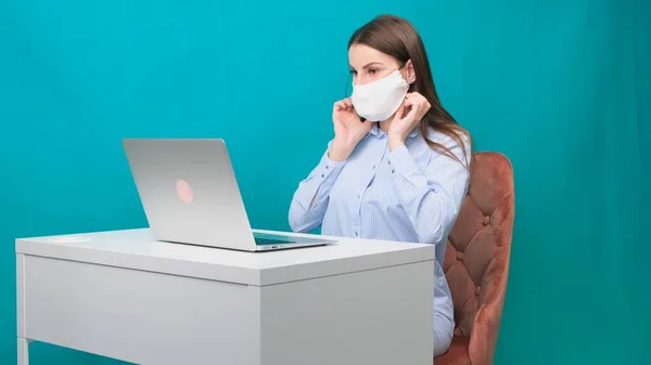 Weibchen setzen sich eine Schutzmaske auf, während sie am Arbeitsplatz oder zu Hause während einer Pandemie an einem Laptop arbeiten. Das Konzept der Arbeit während Quarantäne und Selbstisolierung. — Stockfoto
