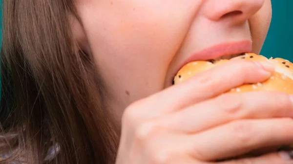 Close-up van een vrouwtje dat een hamburger bijt op een groen scherm. Het concept van ongezonde voeding en voeding. — Stockfoto