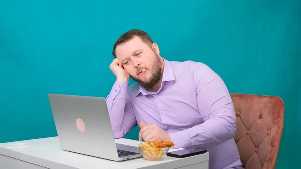 Homem perde um laptop no local de trabalho e come batatas fritas. Conceito freelance, trabalho em casa, fadiga no trabalho, apatia — Fotografia de Stock