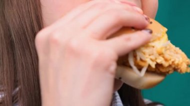 Yeşil ekranda hamburgeri ısıran bir kadının yakın çekimi. Sağlıksız beslenme ve diyet kavramı.