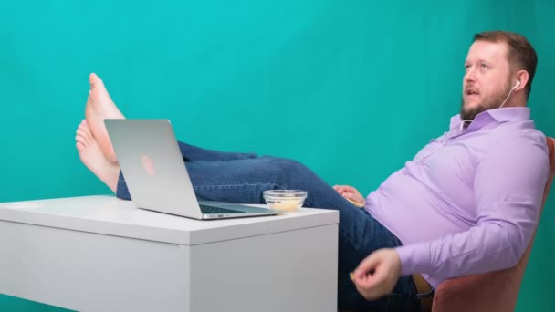 Close-up Empresario perezoso en el lugar de trabajo con las piernas en la mesa comiendo patatas fritas. El concepto de aburrimiento y fatiga en el trabajo — Vídeos de Stock