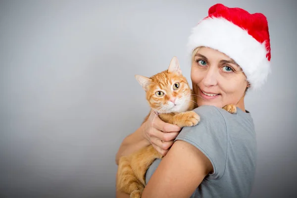 笑着的女人带着圣诞老人的帽子和红猫 — 图库照片