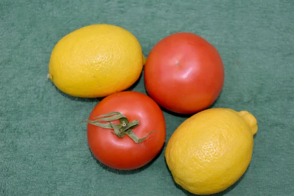 Желтые лимоны и красные помидоры на зеленом . — стоковое фото