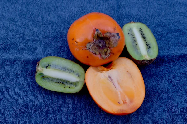 Kiwi and persimmons on a blue table. — Stock Photo, Image
