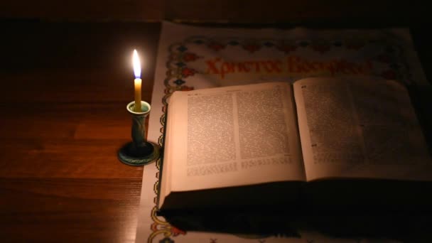 一个孤独的蜡蜡烛在黑暗的房间里燃着 一本打开的书躺在附近 一盏昏暗的灯照亮了圣经的书页 除了那本书 什么也看不见 — 图库视频影像