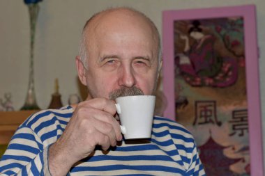 Çizgili tişörtlü bir adam fincandan çay içiyor..