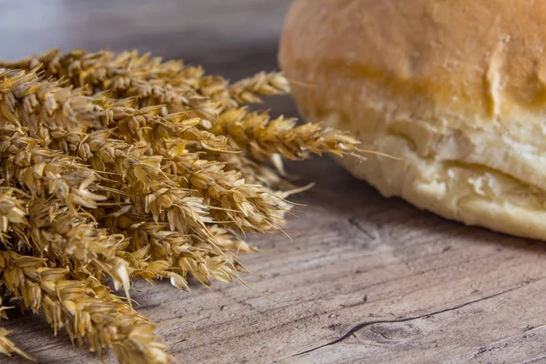 A loaf of bread and ears of ripe wheat lie on a wooden table. — Stock Photo, Image