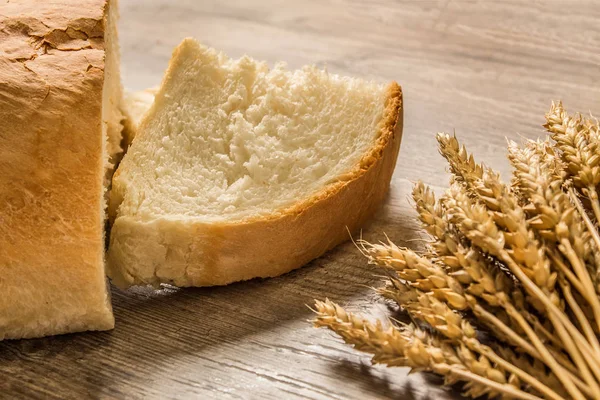 A loaf of bread and ears of ripe wheat lie on a wooden table. Gr — Stock Photo, Image