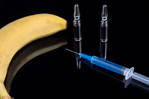 Testing GMO plant in laboratory on banana - biotechnology and GMO concept. GMO genetically modified food. Banana and syringe with blue drug on a black background with ampoules.