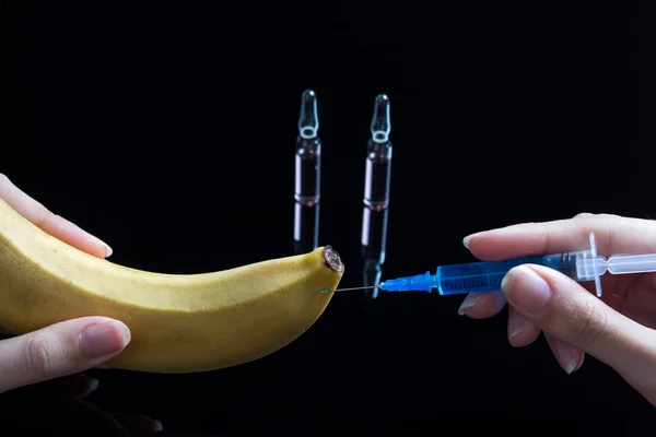 Scientist testing GMO plant in laboratory on a banana-biotechnology and GMO concept.GMO genetically modified food. Hands holding a tomato and a syringe with a blue drug on the background with ampoules