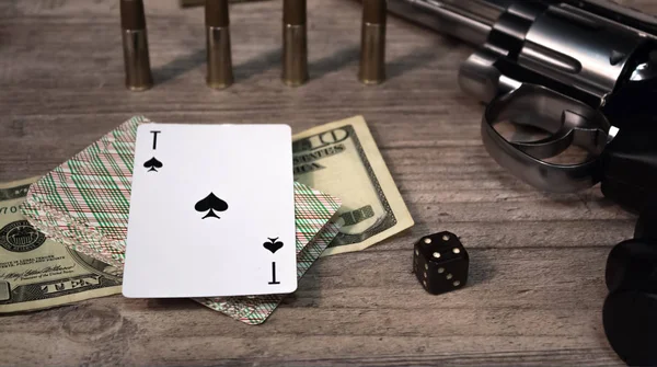 Un juego peligroso por dinero. En una mesa de madera hay una pistola con cartuchos, dólares en efectivo, una baraja de cartas con un as de picas y un dado. Deudas y préstamos de juego peligrosos . — Foto de Stock