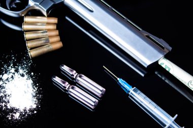 Siyah masada içinde mermi, şırınga ve uyuşturucu bulunan bir tabanca yatıyor. Tehlikeli kötü alışkanlıklar, uyuşturucu ve kumar bağımlılığı. Uyuşturucu yüzünden suç. Bugün uyuşturucu satışı, bulundurmak ve dağıtmak.