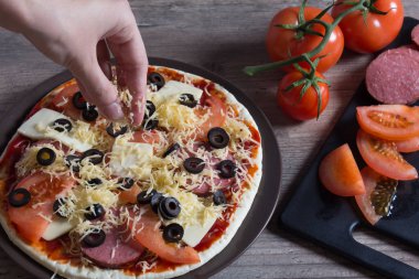 Ellerin pizzaya peynir serpiyor. Domatesli pizza, zeytin ve 