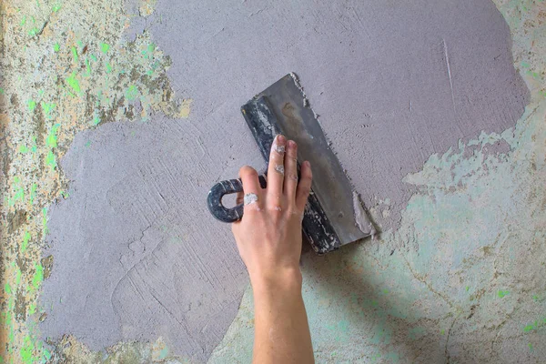 The Builder puts plaster on the wall.Hand holding a spatula with