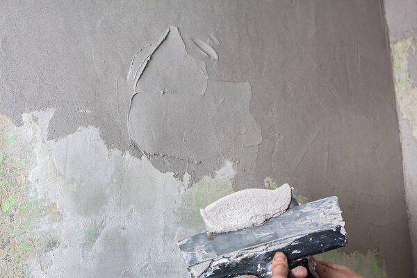 Рука держит шпатель со строительной смесью и разглаживает бу
